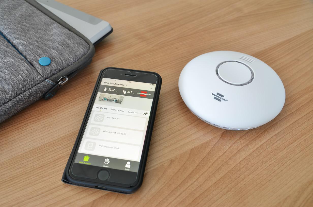 Rilevatore di fumo e calore Brennenstuhl con smartphone app su tavolo legno controllo smart home