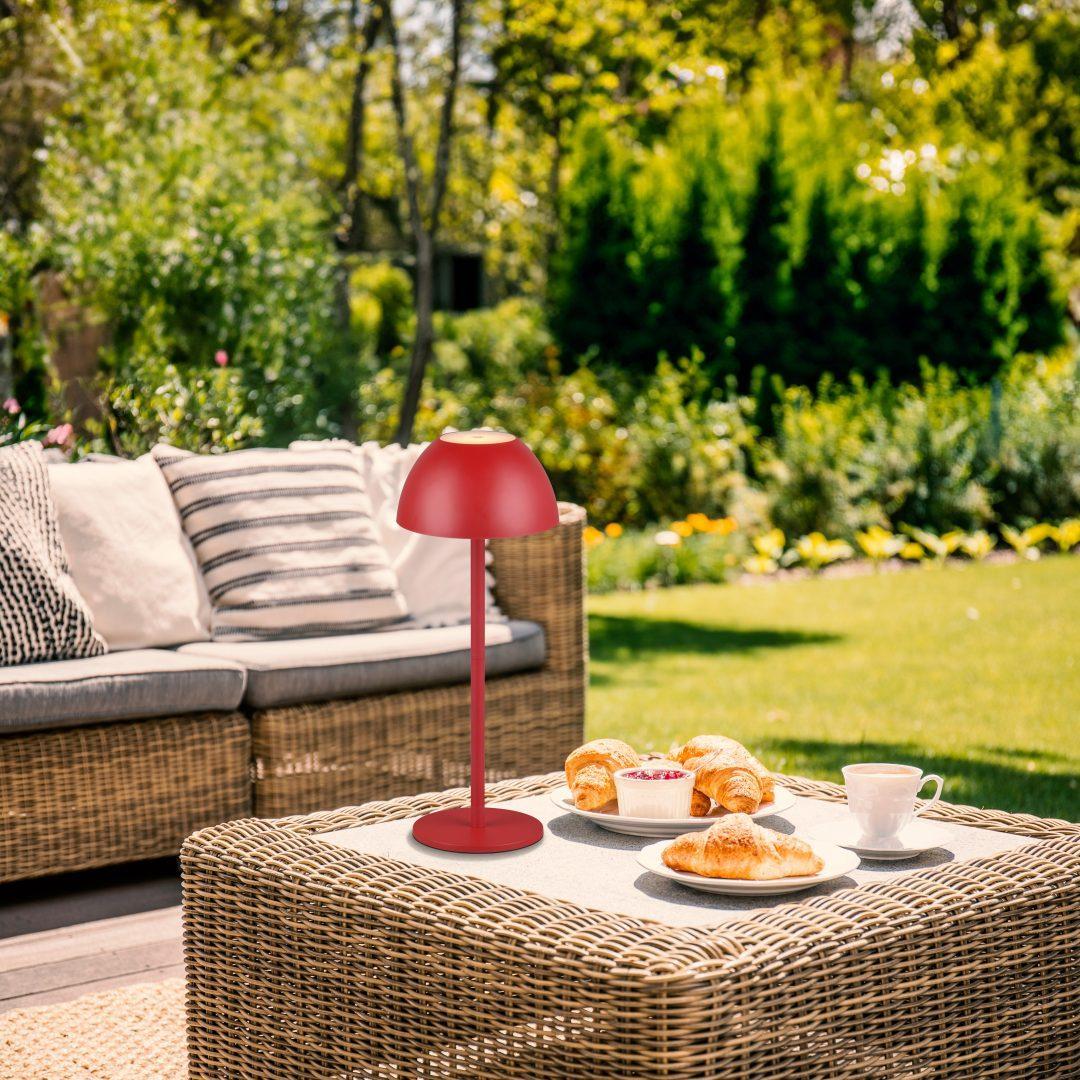 Lampada da tavolo LED touch rossa in plastica per esterno ambientata su tavolino giardino